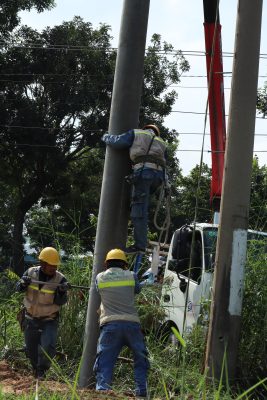 Electrical construction crew rigging a concrete utility pole beside an overhead line route